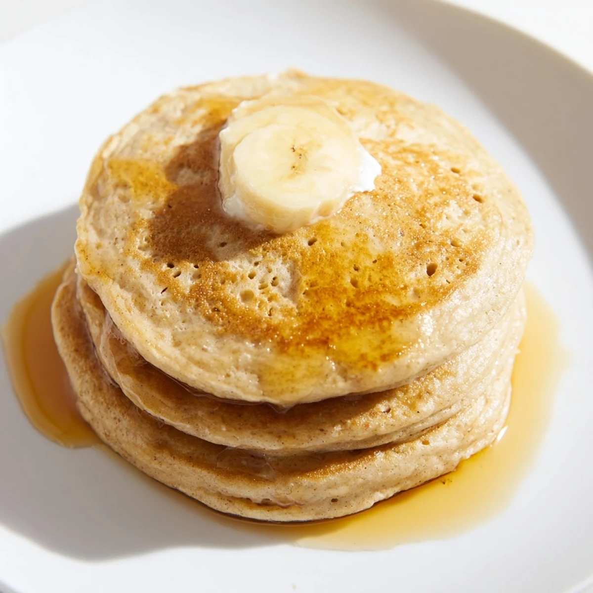 Golden Protein Banana Pancakes, stacked high, ready to be topped with fresh berries and drizzled syrup.
