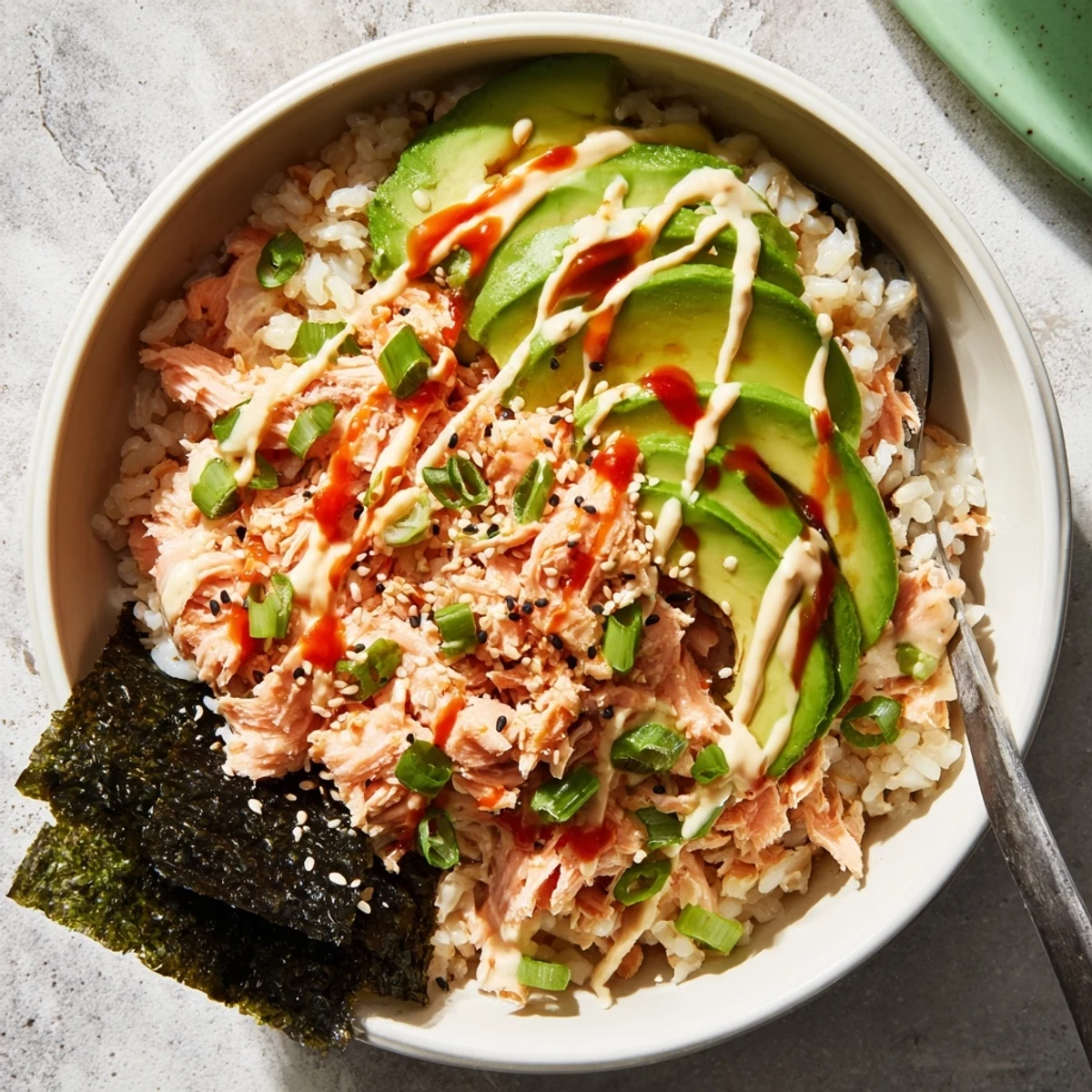 A vibrant Emily Mariko Salmon Rice Bowl with flaked salmon, creamy avocado slices, and spicy mayo drizzle over warm rice.