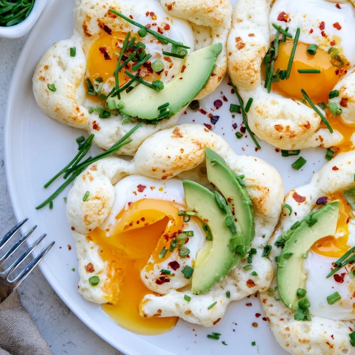 Four golden Cloud Bread Breakfast Clouds, each with a creamy avocado slice and a poached egg nestled in the center, arranged on a rustic wooden board.