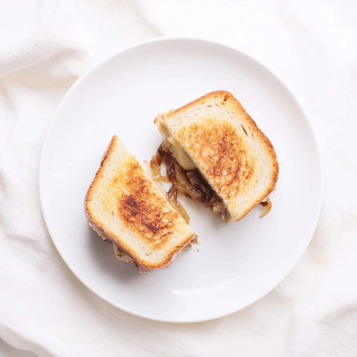 A close-up of a golden, crispy Caramelized Onion & Gruyère Grilled Cheese sandwich sliced in half to reveal gooey cheese.