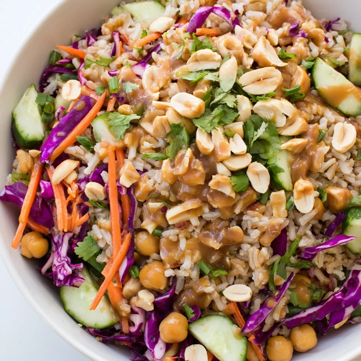 A vibrant Peanut Chickpea Rice Bowl topped with crunchy peanuts, shredded carrots, and red cabbage, drizzled with creamy peanut dressing.