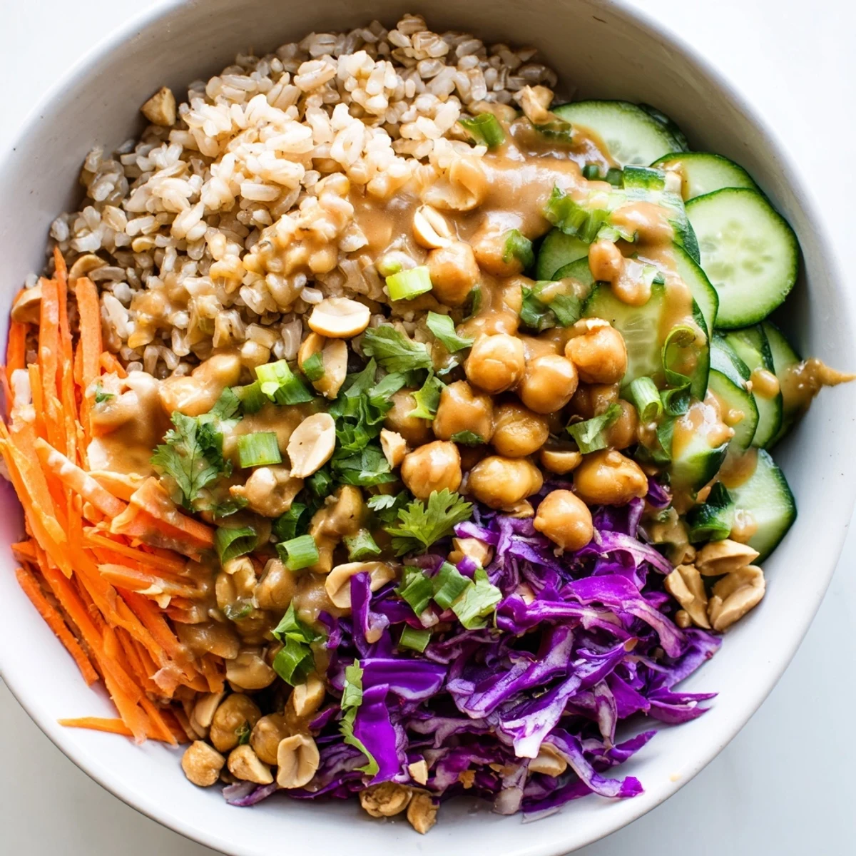 Close-up view of a Peanut Chickpea Rice Bowl, featuring fluffy brown rice, chickpeas, cucumbers, and scallions, all coated in a savory peanut sauce.