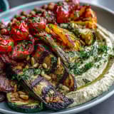 A platter of grilled zucchini, bell peppers, and eggplant paired with smooth, lemony hummus—ideal for Mediterranean-inspired picnics or light summer meals.  