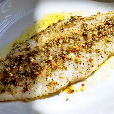 Tender Simple Fork-Friendly Lemon-Herb Tilapia topped with fresh parsley and glistening lemon wedges, a quick meal.