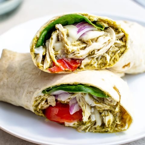 A delicious pesto chicken wrap overflowing with fresh spinach and flavorful roasted peppers.
