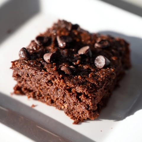 A square of decadent Greek yogurt brownies, topped with melted chocolate chips, ready to eat.