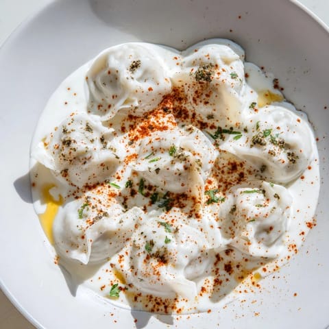 A close-up of golden-brown Turkish Cheesy Manti, swimming in a rich yogurt sauce with spiced butter.