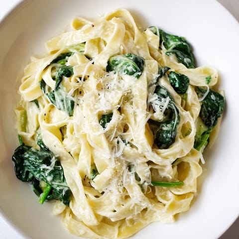 A close-up of Creamy Garlic Spinach Pasta shows garnished parsley and a forkful of saucy noodles and greens.