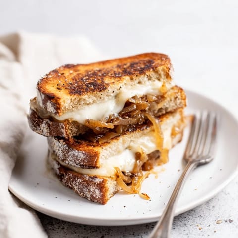 Buttery sourdough grilled cheese filled with jammy caramelized onions and gooey cheddar, served warm alongside a bowl of tomato soup.