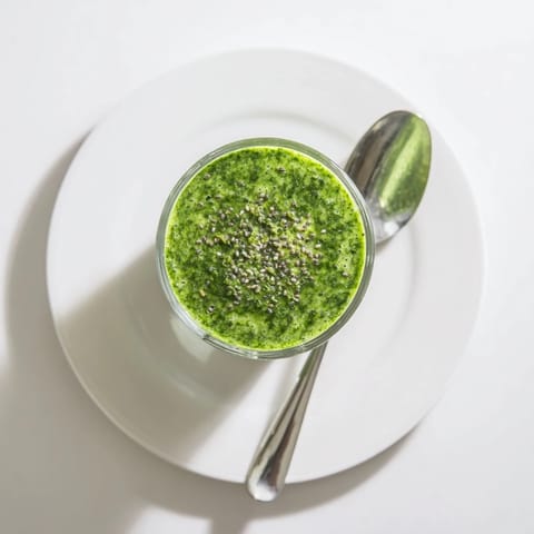 A tall glass of green detox smoothie garnished with mint leaves, blending banana and apple with leafy greens for a refreshing sip.  