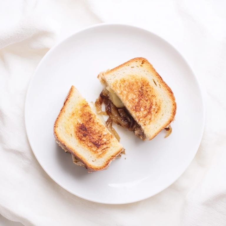A close-up of a golden, crispy Caramelized Onion & Gruyère Grilled Cheese sandwich sliced in half to reveal gooey cheese.
