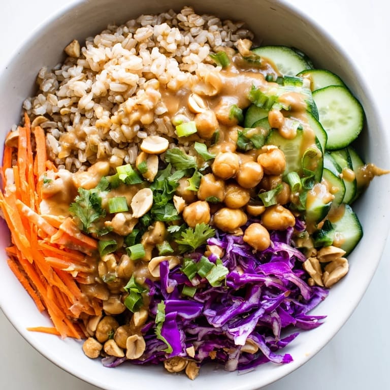 Close-up view of a Peanut Chickpea Rice Bowl, featuring fluffy brown rice, chickpeas, cucumbers, and scallions, all coated in a savory peanut sauce.