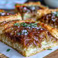 Savory French onion puff pastry tart with caramelized onions, melted Gruyère cheese, and fresh thyme on flaky golden crust.